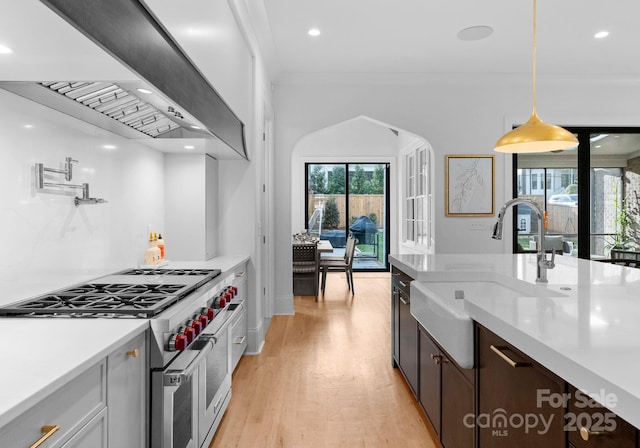 kitchen featuring light wood-type flooring, a sink, double oven range, wall chimney exhaust hood, and light countertops