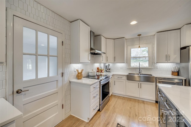 kitchen with white cabinetry, wall chimney range hood, stainless steel appliances, and hanging light fixtures