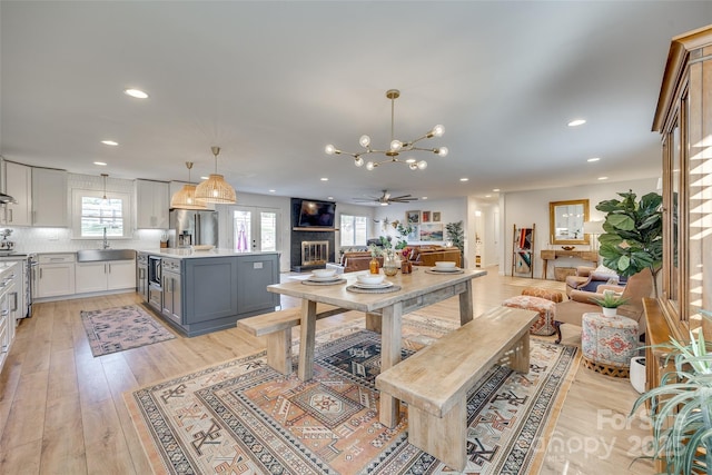 dining area with a fireplace, sink, light hardwood / wood-style floors, and ceiling fan with notable chandelier