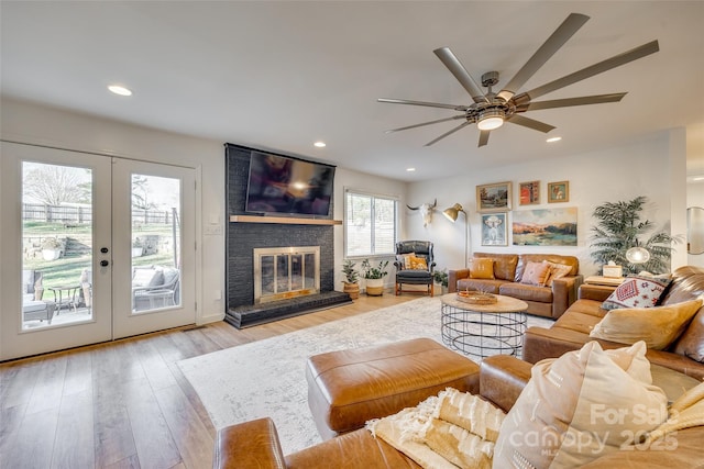 living room featuring french doors, light wood-type flooring, a brick fireplace, and ceiling fan