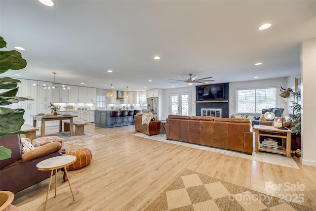 living room featuring ceiling fan with notable chandelier, light hardwood / wood-style floors, and a fireplace