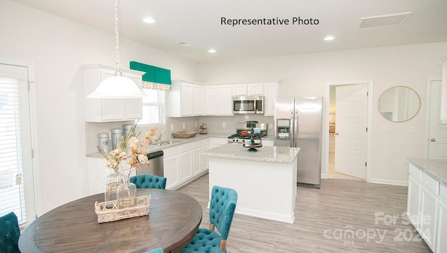 kitchen with white cabinetry, hanging light fixtures, light hardwood / wood-style floors, a kitchen island, and appliances with stainless steel finishes