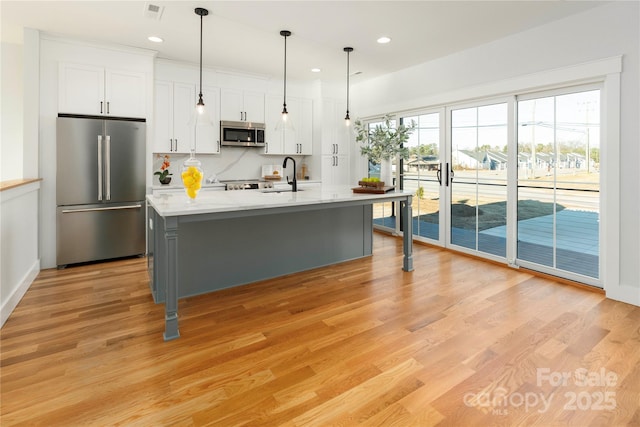 kitchen with appliances with stainless steel finishes, a center island with sink, decorative light fixtures, light hardwood / wood-style floors, and white cabinetry