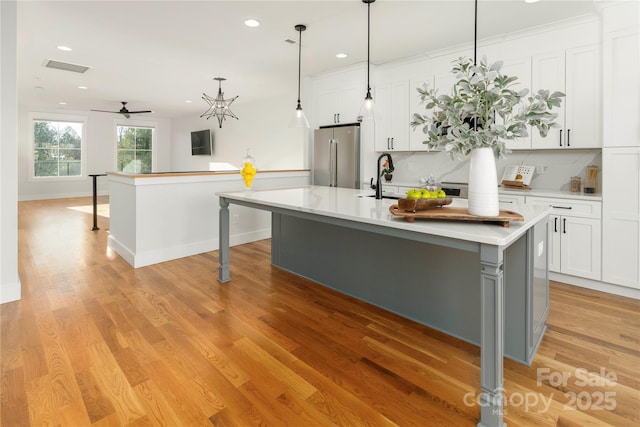 kitchen with decorative backsplash, high end refrigerator, ceiling fan, a center island with sink, and white cabinetry