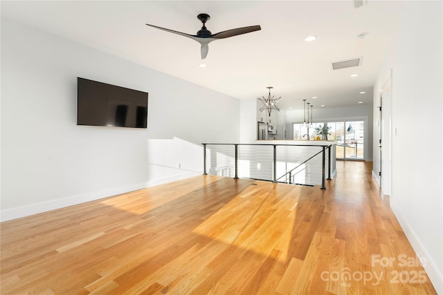 interior space with ceiling fan with notable chandelier and light wood-type flooring