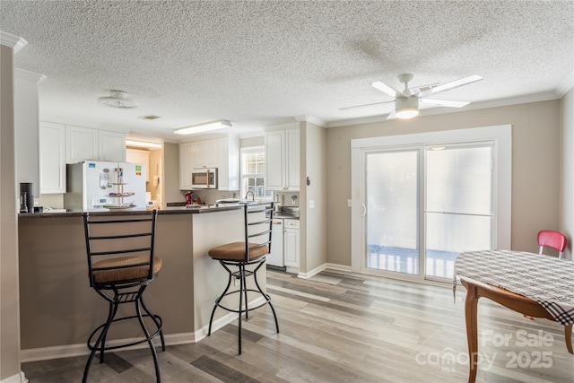 kitchen with kitchen peninsula, ornamental molding, white fridge, white cabinetry, and a breakfast bar area