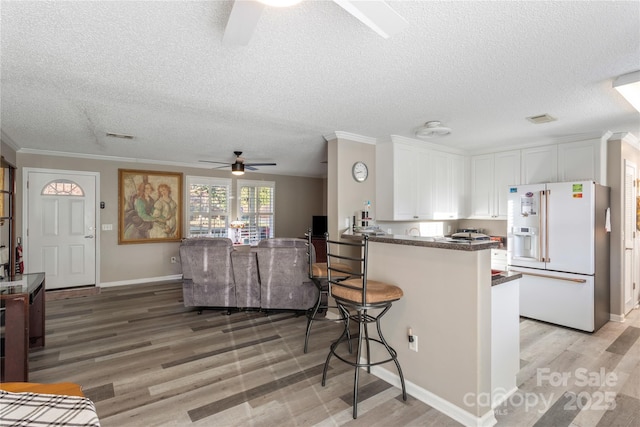 kitchen featuring ceiling fan, white fridge with ice dispenser, kitchen peninsula, white cabinets, and light wood-type flooring