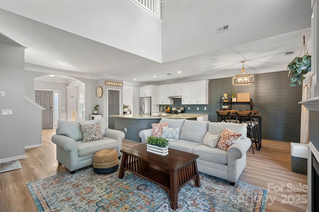 living room featuring a towering ceiling, ornamental molding, light hardwood / wood-style floors, and a notable chandelier