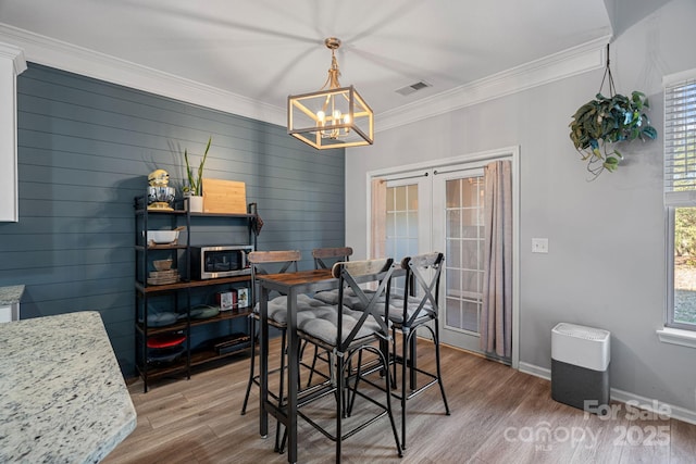 dining area with a notable chandelier, hardwood / wood-style floors, a healthy amount of sunlight, and crown molding