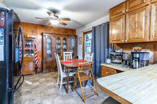 kitchen featuring black refrigerator, ceiling fan, and wood walls