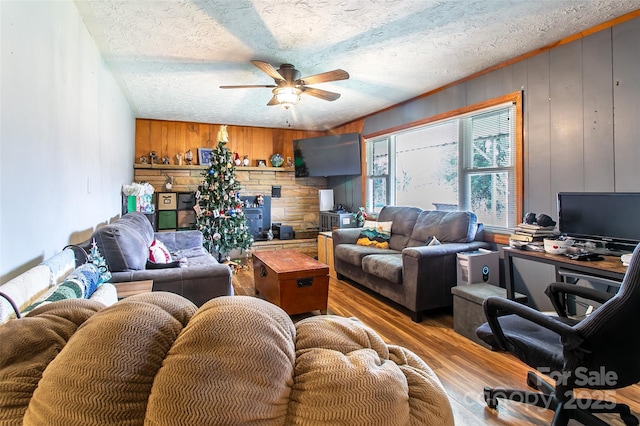 living room featuring light wood-type flooring, ceiling fan, a textured ceiling, and wood walls