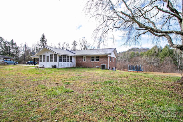 view of front of property featuring metal roof, a trampoline, cooling unit, a front lawn, and brick siding