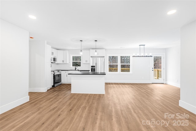 kitchen with white cabinets, hanging light fixtures, tasteful backsplash, light hardwood / wood-style floors, and stainless steel appliances