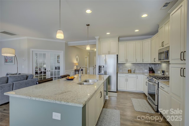 kitchen featuring light stone countertops, stainless steel appliances, sink, hanging light fixtures, and an island with sink