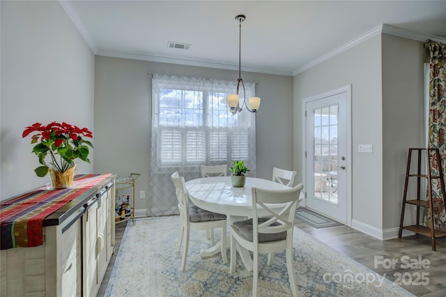 dining space with light hardwood / wood-style flooring, crown molding, and a notable chandelier