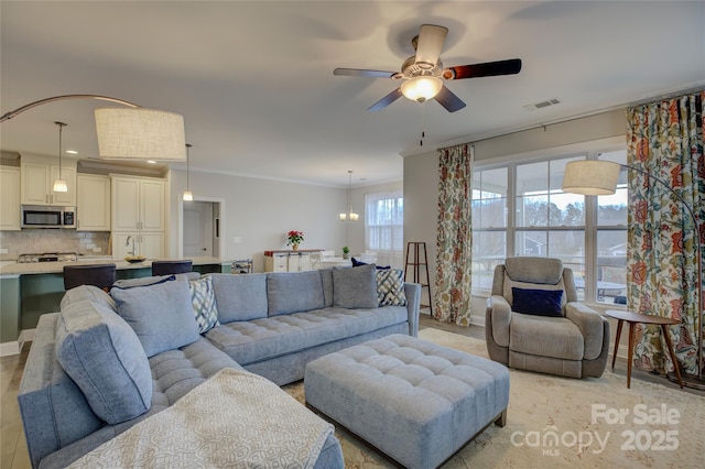 living room with ceiling fan with notable chandelier and ornamental molding