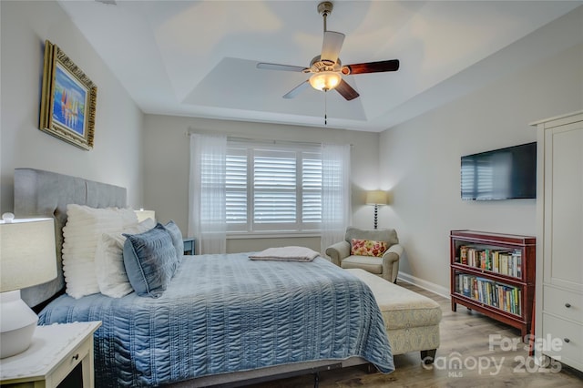 bedroom with ceiling fan, light hardwood / wood-style floors, and a tray ceiling