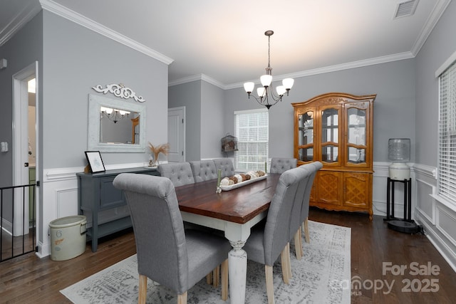 dining space with dark wood-type flooring, ornamental molding, and a notable chandelier