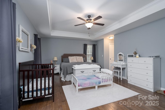 bedroom with a raised ceiling, ceiling fan, crown molding, and dark hardwood / wood-style floors