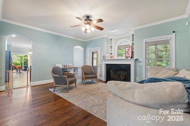 living room featuring a tiled fireplace, ceiling fan, dark wood-type flooring, and ornamental molding