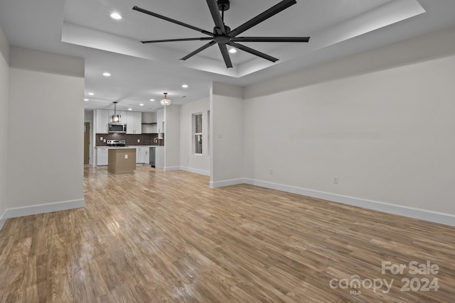 unfurnished living room with light hardwood / wood-style flooring, a raised ceiling, and ceiling fan