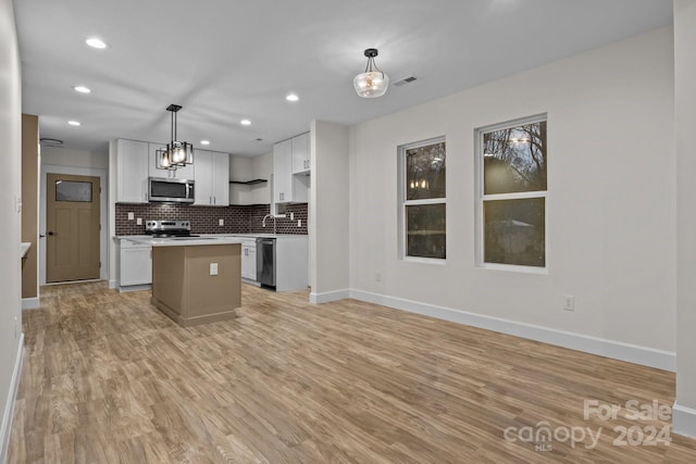 kitchen with light hardwood / wood-style flooring, appliances with stainless steel finishes, decorative light fixtures, a kitchen island, and white cabinetry