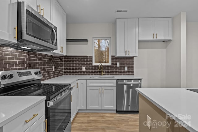 kitchen with sink, decorative backsplash, light hardwood / wood-style floors, white cabinetry, and stainless steel appliances