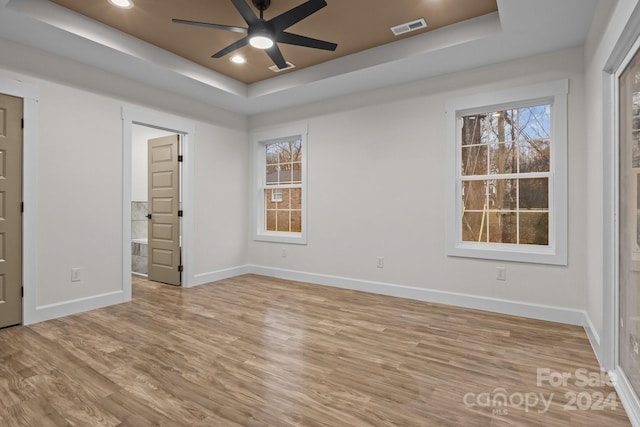 unfurnished bedroom featuring light wood-type flooring, ensuite bath, a raised ceiling, and ceiling fan