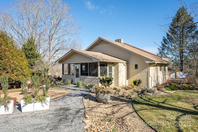 view of front of house featuring a shingled roof, a front lawn, aphalt driveway, a chimney, and a sunroom