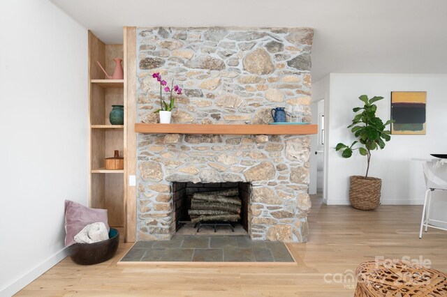 interior details featuring built in shelves, baseboards, a stone fireplace, and wood finished floors