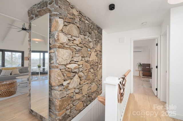 hall with light wood finished floors, an upstairs landing, an AC wall unit, and lofted ceiling with beams