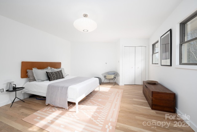 bedroom with a closet, light wood-style flooring, and baseboards