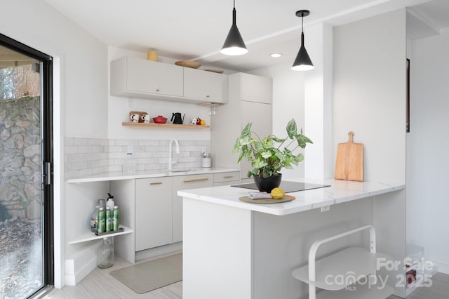 kitchen with open shelves, black electric stovetop, a breakfast bar area, a peninsula, and a sink