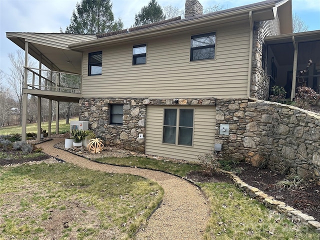 rear view of property featuring ac unit, stone siding, and a chimney