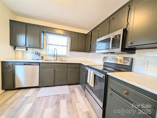 kitchen with tasteful backsplash, a textured ceiling, stainless steel appliances, sink, and light hardwood / wood-style floors