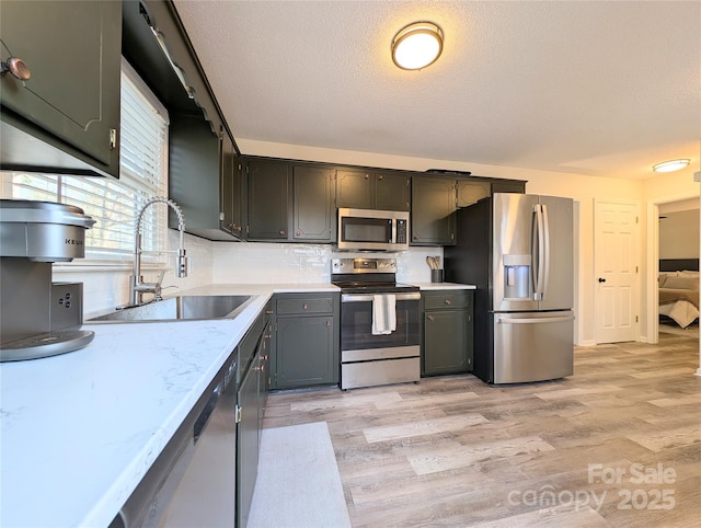 kitchen featuring backsplash, sink, a textured ceiling, light hardwood / wood-style floors, and stainless steel appliances