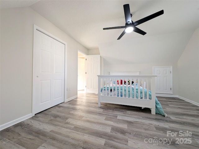 unfurnished bedroom featuring ceiling fan, light hardwood / wood-style floors, vaulted ceiling, a closet, and a crib