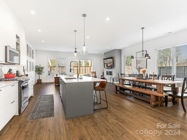 kitchen with pendant lighting, a kitchen island with sink, white cabinets, sink, and stainless steel appliances