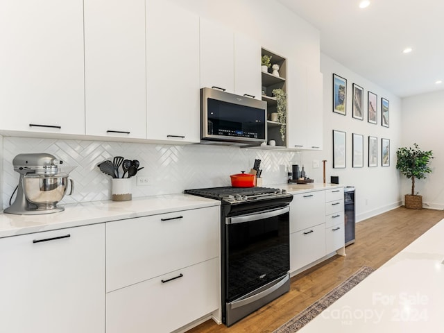 kitchen featuring backsplash, white cabinets, light hardwood / wood-style flooring, appliances with stainless steel finishes, and light stone counters