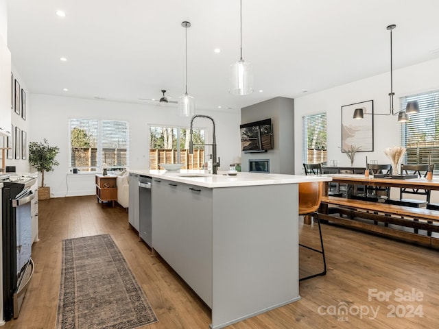 kitchen with sink, a center island with sink, hanging light fixtures, and appliances with stainless steel finishes