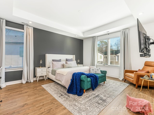 bedroom featuring a tray ceiling, multiple windows, and wood-type flooring