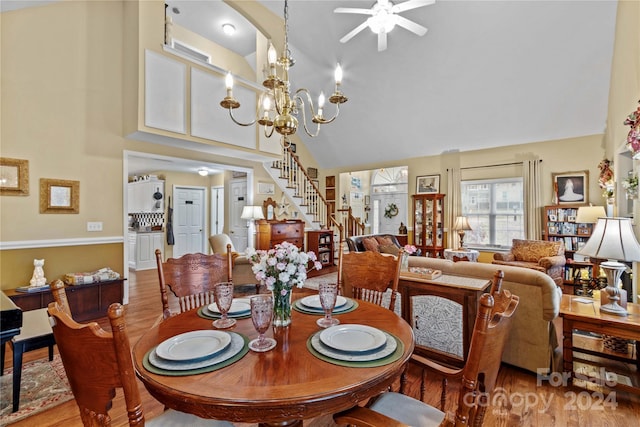 dining space with ceiling fan with notable chandelier, high vaulted ceiling, and light hardwood / wood-style flooring