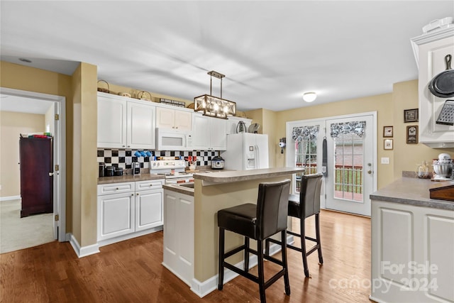 kitchen featuring decorative backsplash, a kitchen breakfast bar, white appliances, decorative light fixtures, and white cabinets