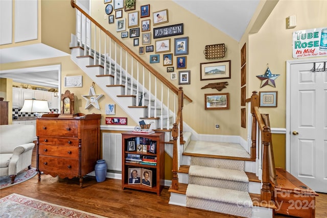 staircase with hardwood / wood-style floors and high vaulted ceiling