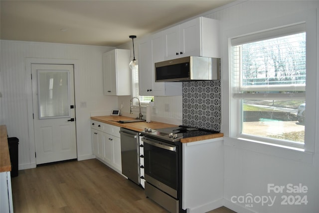 kitchen with wood counters, white cabinets, sink, decorative light fixtures, and stainless steel appliances