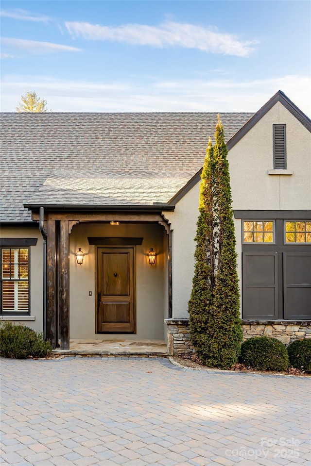 entrance to property with stucco siding and roof with shingles