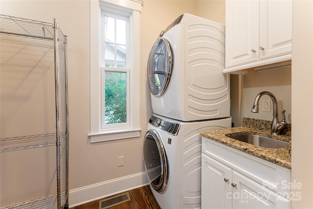 clothes washing area with visible vents, cabinet space, stacked washer and clothes dryer, and a sink