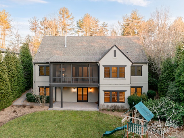 rear view of property featuring a patio, stucco siding, a lawn, a sunroom, and a shingled roof