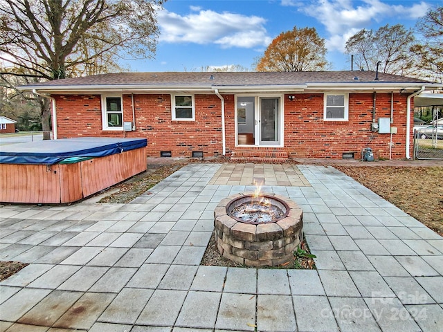 rear view of property featuring a fire pit, a patio area, and a hot tub