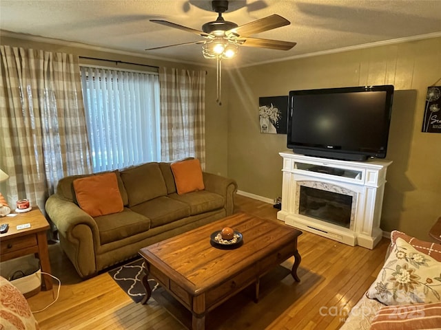 living room featuring crown molding, ceiling fan, a fireplace, a textured ceiling, and light wood-type flooring